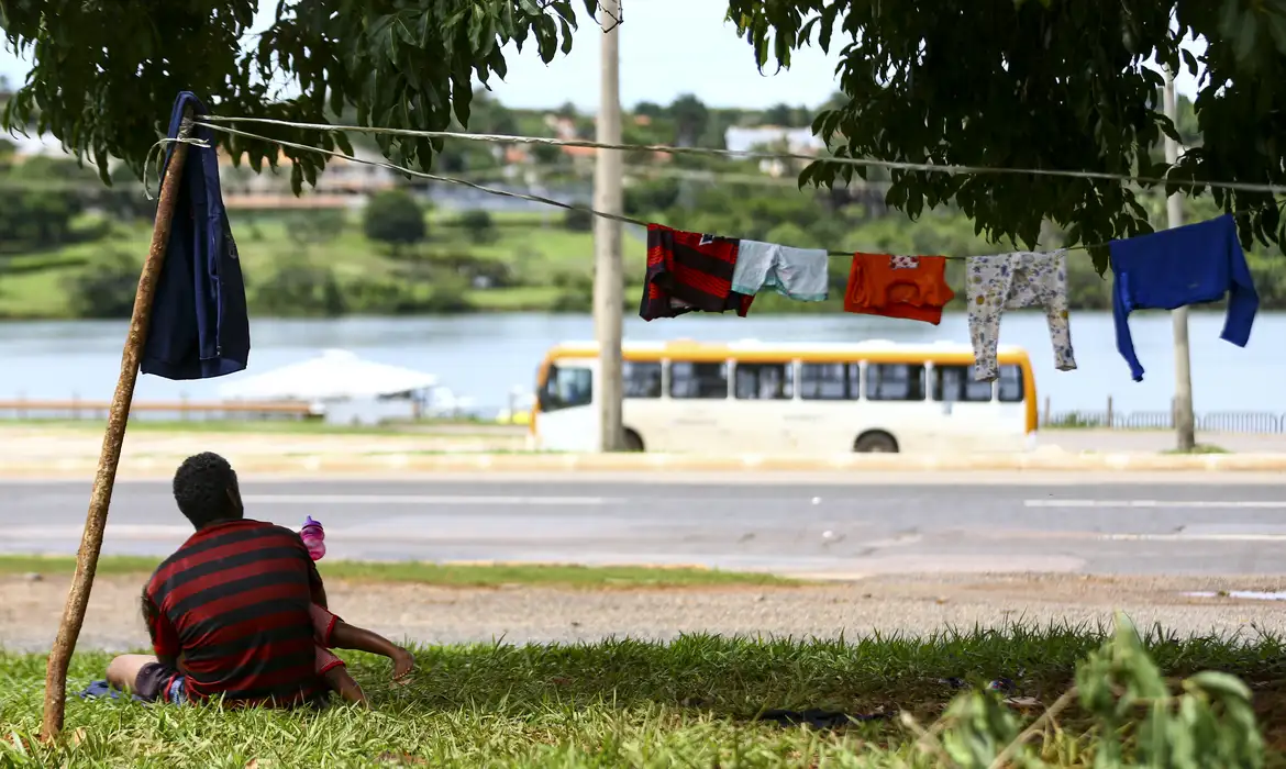 Imagem de uma pessoa sentada na grama em situação de vulnerabilidade